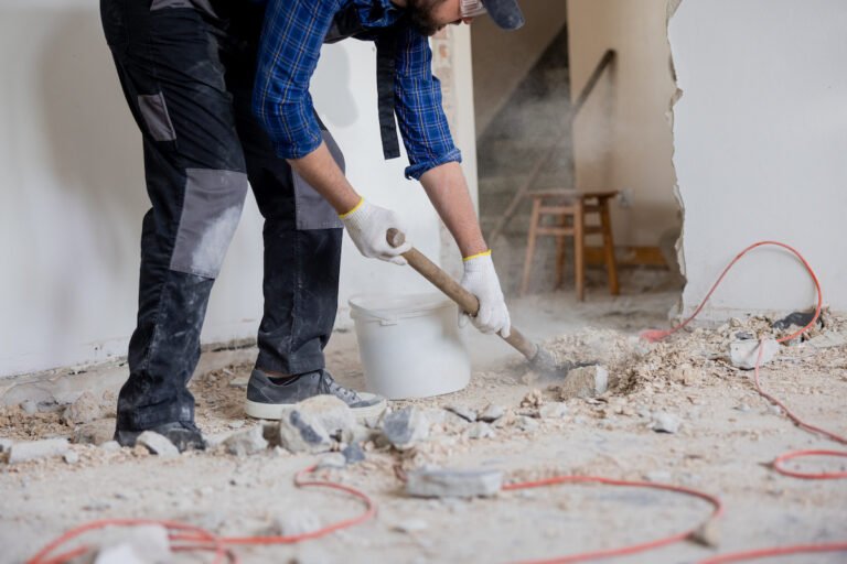 Close up shot of the legs of a man in a protective suit with a shovel in hand next to a bucket of debris left over from a house renovation